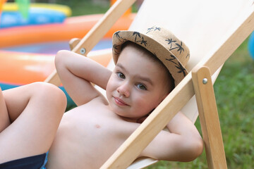 A cute little child is relaxing in a sun lounger near an inflatable pool. Summer vacation outdoors,...