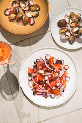 Saute with clams (Venus clams or vongole) and salad with octopus and tomato served with rose wine. Summer Mediterranean seafood cuisine on a textured background  tiles, top view, bright singligt