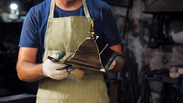Close-up of a restorer in a work apron applying paint to a decorative street lamp in the workshop.