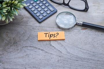 The words Tips written on the post-it note with a magnifying glass, calculator and eyeglasses on the wooden table