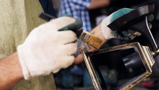 Close-up of a man in white gloves restoring the frame of a decorative street lamp. A master restorer applies paint to the forged frame of a street lamp.