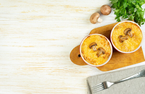 Chicken and mushroom casserole with golden crust, julienne with baked cheese, creamy gratin in portion ramekin clay pot on white wooden background. French cuisine. Top view, flat lay with copy space