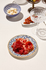 Meat antipasti on ceramic plate on white table with hard shadow. Meat platter with bresaola, hamon, prosciutto. Meat appetizer in Italian menu. Aesthetic food composition. Sunny day in tuscany.