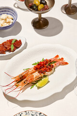 Seafood appetizer - baked langoustines with tomato tartar on white table. Grilled shrimp in italian restaurant menu. Langoustines on white background with shadows. Shrimp appetizer. Baked prawn.