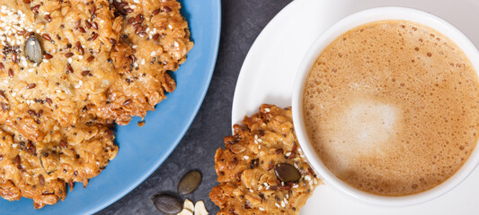 Cup of coffee with milk and fresh baked oatmeal cookies on blue plate. Delicious crunchy dessert
