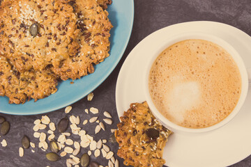 Cup of coffee with milk and fresh baked oatmeal cookies with honey and healthy seeds. Delicious crunchy dessert