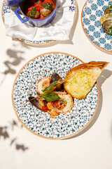 Seafood platter with cooked shrimps, mussels, sea scallops in tomato sauce on white table. Stew seafood in italian style with ciabatta bread. Seafood dish: prawns, shellfish, scallops