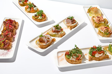 Fototapeta na wymiar Aesthetic composition with bruschetta on white background over white wall. Set of bruschetta with shrimp, salmon, beef, tomatoes and crab on fine dining in summer. Elegant menu concept.