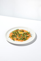 Salmon carpaccio with arugula on white background in summer day. Fish appetizer - salmon carpaccio in fine dining with shadows. Elegant carpaccio of raw salmon and sauce. Italian food. Aesthetic menu.