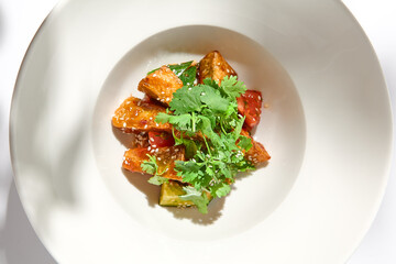 Crispy eggplant in chinese style on white plate. Crispy eggplant salad on summer menu. Asian appetizer - roasted aubergine with coriander leaves. Vegan food. Aesthetic veggie menu.