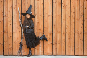 Cute teenager girl with brunette long hair in halloween black witch costume, hat and a broom...