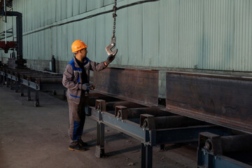 Worker receiving a metal bar from crane in warehouse