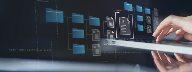 Document Management System (DMS) being setup by IT consultant working on laptop computer in office with document directory. Software for archiving, searching and managing corporate file information