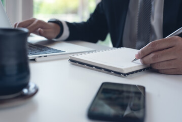 Businessman writing on notebook and working on laptop computer at office. Business man planning his work on notepad on office table