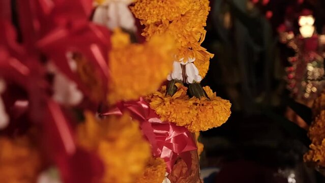 Close up marigold wreath flowers in Asian temple, orange colors with red ribbons and some other flowers dark temple with some statues in the background, slow motion, High quality FullHD footage