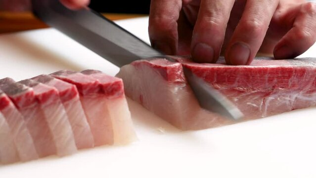 和食レストランの厨房で、熟練の職人が包丁で丁寧に切り分ける新鮮なカンパチの刺身。シズル感あふれる調理シーンの動画素材