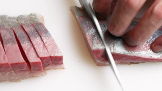まな板の上で、新鮮なカンパチの身を包丁で丁寧に切り分ける動作。脂の乗った断面と、手際よく刺身や切り身にしていく様子を捉えたクローズアップ映像。飲食店メニュー、海鮮料理の紹介、和食や調理技術をテーマにした広告素材に。 | Cutting fresh amberjack (Kanpachi) into slices on a cutting board.