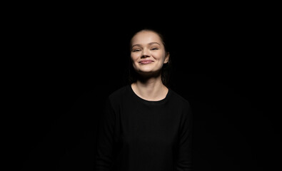 Portrait of emotive good-looking brunette woman looking in a camera and standing against black background.