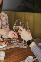 Two young woman clinking glasses with wine over served table with food in cafe or restaurant. Close-up hands with wineglasses