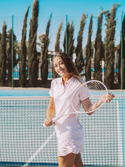 Mujer joven sonriente usando una raqueta de tenis en una pista de tenis al aire libre durante las vacaciones de verano