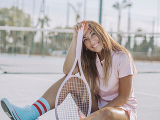 mujer joven sentada en el suelo con una raqueta de tenis