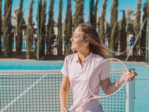 Mujer joven sonriente usando una raqueta de tenis en una pista de tenis al aire libre durante las vacaciones de verano