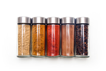 The different types of spices and herbs stored inside the small closable glass bottle isolated on a white background. 