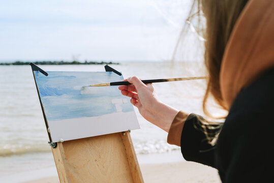 Faceless shot of a female drawing on a beach. en plein air artist