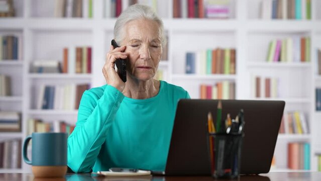 Senior woman with laptop computer calling on smartphone at home technology, communication and people concept, happy elderly woman