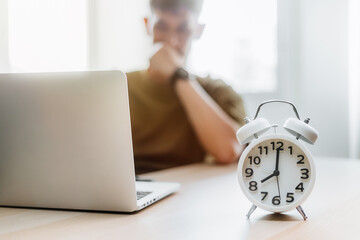 Alarm clock on the desk. Man contemplating work in modern office building or home at morning using laptop.
