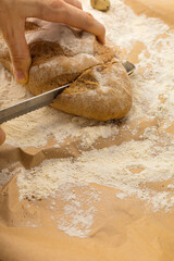 Man's hands cut a fresh wheat bun with a bread knife