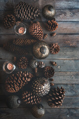 Sustainable elegant christmas decoration on dark vertical wooden background with pine cone, candle lights and christmas balls. Top view with space for text.