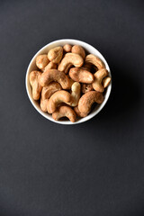 Delicious cashew nuts in a ceramic bowl on a black background. Delicious breakfast of nuts.