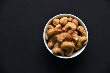 Delicious cashew nuts in a ceramic bowl on a black background. Delicious breakfast of nuts.