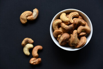 Delicious cashew nuts in a ceramic bowl on a black background. Delicious breakfast of nuts.