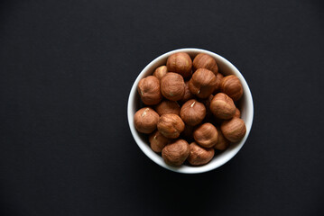 Delicious hazelnuts in a ceramic bowl on a black background. Delicious breakfast of nuts.