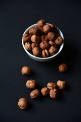 Delicious hazelnuts in a ceramic bowl on a black background. Delicious breakfast of nuts.