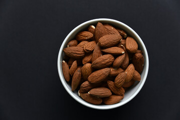 Delicious almonds in a ceramic bowl on a black background. Delicious breakfast of almonds.