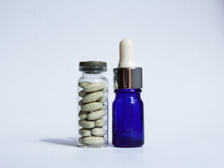 Closed glass jars with green pharmaceutical pills and blue pipette with a drops for health care on a white background 