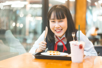  Happy young asian woman in japanese uniform student at cafe with waffle