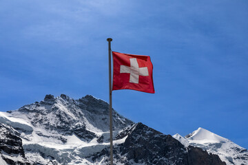 Flag of Switzerland with the top of the Jungfrau mountain behind it. 