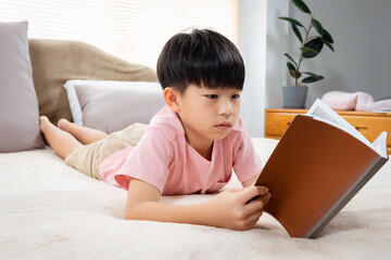 9-year-old Asian boy sitting and reading a book With pleasure, he readily reviewed the things he had learned each day in his bed in the bedroom of the house.