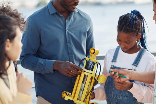 Cropped shot of black male teacher demonstrating robot model to group of children outdoors