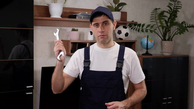 Handsome young man wearing builder jumpsuit uniform and holding wrench.