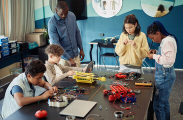 Diverse group of teenage children building robots together while enjoying engineering class in...