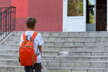 A happy smiling child goes to school. Back view of boy walking on stairs outdoors building background. A student goes to study with a backpack. Back to school