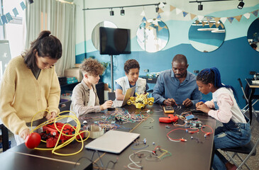 Diverse group of children building robots with male teacher helping during engineering class at...