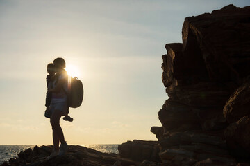 mother carry her son at natural stone arch in beach at sunset