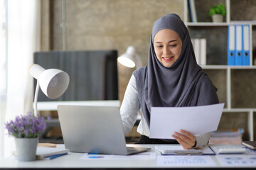 Attractive muslim businesswoman in office working on laptop and reading documents.