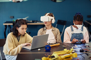 Diverse group of children building robots in engineering class and using VR technology